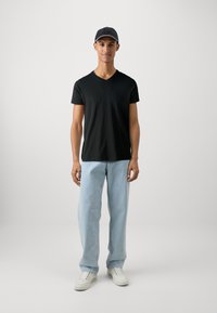 Czarny t-shirt z dekoltem w serek, jasnoniebieskie jeansy proste, białe sneakersy i ciemna czapka. Strój charakteryzuje się prostymi fasonami i neutralnymi kolorami.