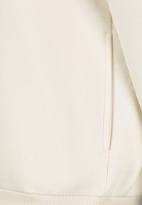 Creme-kleurige sweatshirt met een gladde textuur, ribgebreide manchetten en een discreet zijvak op de linkernaad.