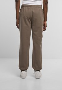 Braune Sweatpants mit einem elastischen Bund, lässiger Passform und strukturiertem Stoff. Verfügen über ein einfaches Design und werden mit weißen Turnschuhen kombiniert.