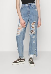 Høyt liv blå denimjeans med flere rifter og flagrende kanter. Kombinert med rutete sneakers, som gir et avslappet utseende.