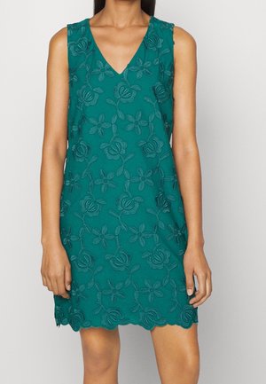 Robe sans manches bleu sarcelle avec broderie florale, col en V et ourlet festonné portée par une personne sur un fond clair uni.