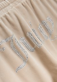 Beige fluweel stof met rhinestone versieringen die "Juni" spelllen. De textuur is zacht, met een gladde, glanzende uitstraling door de kristallen.