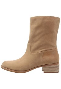 Bottine en daim couleur fauve avec un bout rond, une tige sans coutures et un talon superposé orné d'un détail en anneau texturé. Texture lisse sur toute la surface.