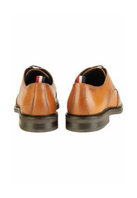 Braune Leder Schuhe mit einer glatten Oberfläche, runder Zehenform und einer kontrastierenden dunklen Sohle. Mit einer hinteren Zuglasche mit roten, weißen und blauen Akzenten.