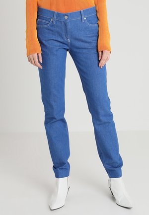 Blauwe denim jeans met een getailleerd ontwerp, vijf zakken en zichtbare stiksels. Gekocht met een gestructureerde oranje top en witte laarzen.