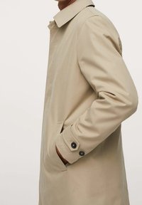 Trench beige au design simple, doté d'un col, de poches latérales et de détails de poignets boutonnés. Texture lisse, coupe longueur genoux.