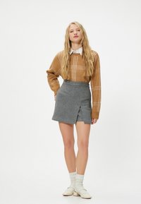 Brauner Strickpullover mit karierter Musterung, kombiniert mit einem grauen Woll-Minirock mit einem Schlitz vorne. Darunter ein weißes Hemd mit Kragen.