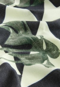 Abstraktes gemustertes Gewebe mit grünen Formen auf einem schwarz-weißen Hintergrund, mit weicher Textur und glatter Oberfläche.