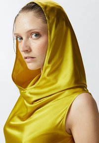 Maglietta con cappuccio in satin gialla con scollatura drappeggiata, caratterizzata da una texture morbida e un design aderente, che esalta il viso e le spalle.