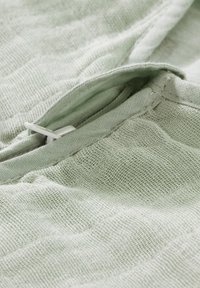 Light green, textured fabric with a soft, woven appearance. Features a partially visible zipper with a white pull tab.
