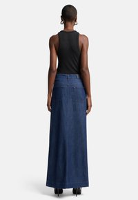Maxi denimskjørt med mørkeblå vask, høy midje, to baklommer og beige sømdetaljer. Brukt med en ermeløs svart topp.