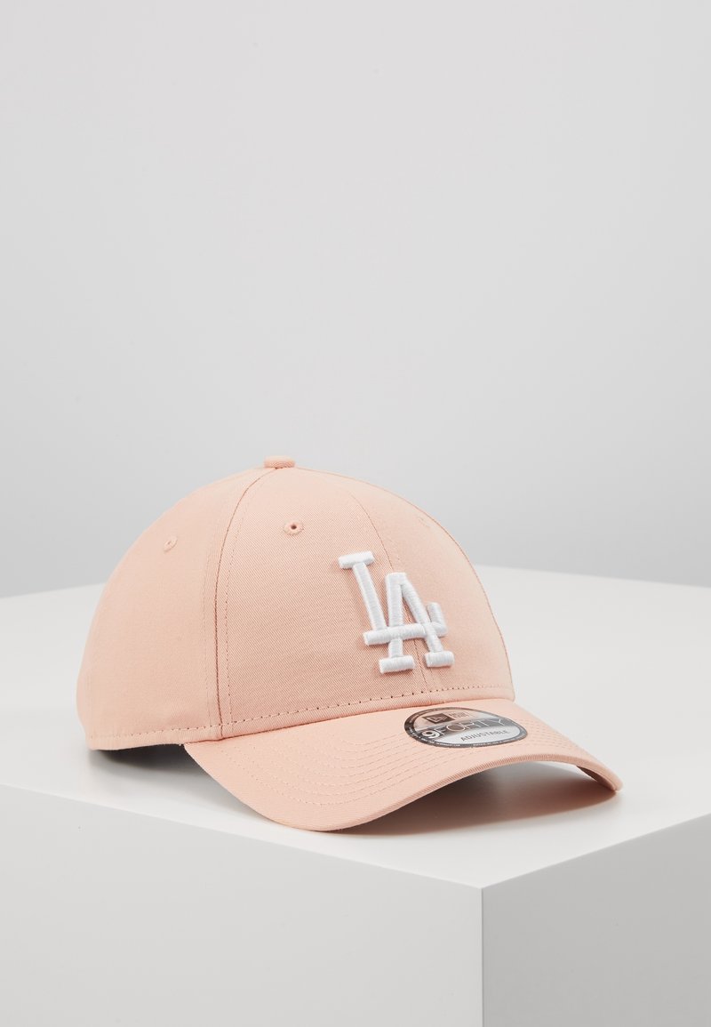Casquette de baseball rose clair avec logo "LA" blanc brodé à l'avant, posée sur une surface blanche devant un fond gris uni.