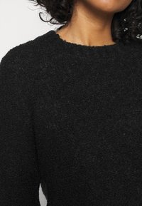 Pull noir texturé avec une finition douce et duveteuse ; présente un col rond et des manches longues, offrant un look chaleureux et confortable.