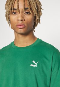 Grøn bomulds T-shirt med rund hals, prydet med et hvidt Puma-logo på venstre bryst. Glat tekstur med en afslappet pasform.