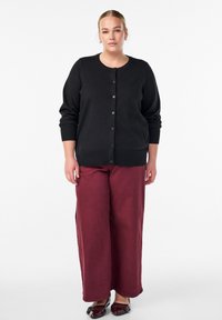 Schwarzer Cardigan mit rundem Ausschnitt und Knöpfen vorne, kombiniert mit weitem burgunderroten Hosen. Glatte Textur mit gerippten Bündchen.