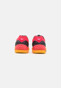 Baskets de sport rouges et noires avec une surface texturée, un talon rembourré et une semelle extérieure orange. Présente le logo Mizuno à l'arrière.