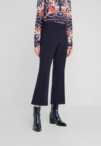 Námořnické zvonové kalhoty vyrobené z pevné látky. Mají hladký povrch a přiléhavý střih, doplněné lesklými námořnickými kotníkovými botami.