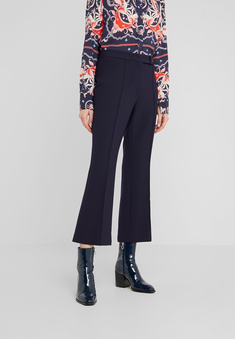 Námořnické zvonové kalhoty vyrobené z pevné látky. Mají hladký povrch a přiléhavý střih, doplněné lesklými námořnickými kotníkovými botami.