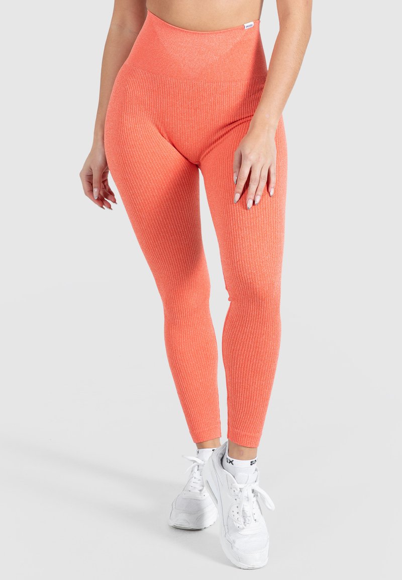 Leggings a vita alta a coste in un vivace corallo, con un design senza cuciture e tessuto elastico texturizzato. Indossati con sneakers bianche.