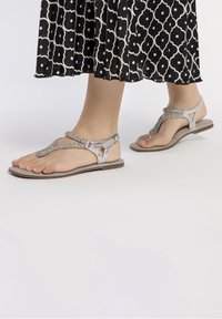 Sølv flade sandaler med teksturerede stropper og spænde lukning. Sålen er lys beige, og designet har en åben tå stil.