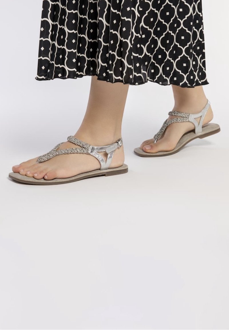 Sølv flade sandaler med teksturerede stropper og spænde lukning. Sålen er lys beige, og designet har en åben tå stil.