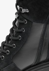 Schwarzer Schnürstiefel aus einer Kombination von Wildleder und Leder, mit glänzender Oberfläche und seitlichem Reißverschluss für einfaches An- und Ausziehen.