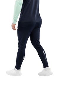Navyfarbene Sporthose mit einem schlanken Design, ausgestattet mit weißen Akzentknöpfen an der Seite und einer taillierten Form, kombiniert mit weißen Sneakers.