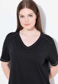 Sort V-hals t-shirt med korte ærmer, der har hvide syninger langs halsudskæringen og skuldersømmene. Blød, glat tekstur.