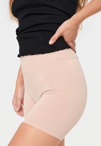 Ljust rosa stretchmaterialshorts med hög midja, slät struktur och figurnära design, kombinerat med en ribbad svart topp.