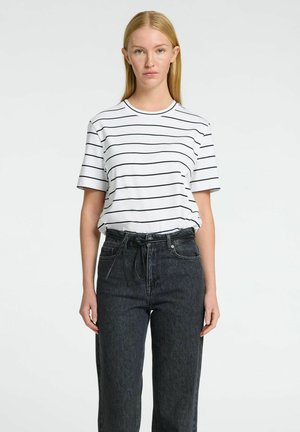 T-shirt bianca con righe orizzontali nere, maniche corte, scollatura rotonda, abbinata a jeans in denim scuro a vita alta con cintura.