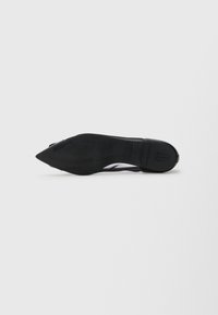 Chaussure noire à bout pointu avec une tige en cuir lisse et un talon fin. La semelle est plate avec une empreinte de logo discrète. Design minimaliste.