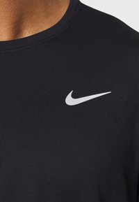 Schwarzes Sportshirt mit rundem Halsausschnitt und kurzen Ärmeln. Verfügt über ein weißes Nike-Logo im linken Brustbereich. Glatte Textur.