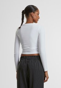 Hvit langermet topp med en tettsittende design og en cropped hem, kombinert med svarte bukser med pinstriper og elastisk liv.