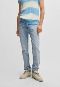 Jeans in denim azzurro chiaro, modello a gamba dritta, abbinati a un maglione senza maniche a righe azzurro chiaro e bianco e sneakers beige.