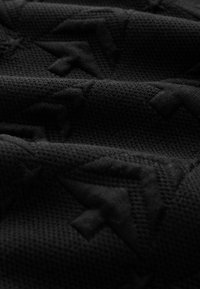 Sort struktureret stof med et subtilt mønster af hævede geometriske former, der viser et netlignende væv og en glat overflade.