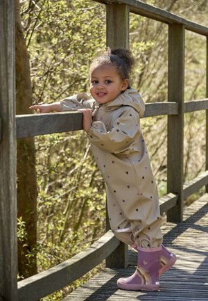 Beige waterdicht overal met kleine zwarte en paarse hartpatronen, gecombineerd met lichtpaarse rubberen laarzen met een gestreept ontwerp.