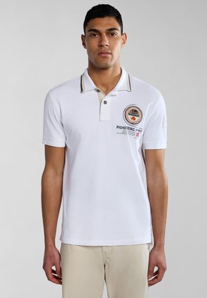 Polo bianco con colletto beige, caratterizzato da un ricamo con patch e testo sul lato sinistro del torace. Maniche corte e una texture morbida in cotone.