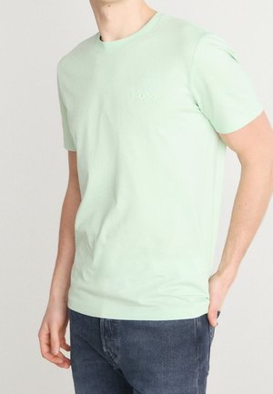 Hellgrünes Baumwoll-T-Shirt mit Rundhalsausschnitt und kurzen Ärmeln; mit geprägtem "BOSS"-Logo auf der Brust. Kombiniert mit dunklen Jeans.