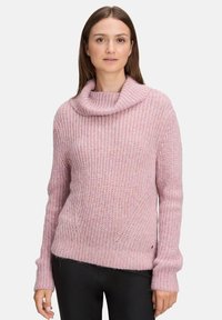Rosa gestrickter Pullover mit einem Kragen, der eine strukturierte Musterung und überschnittene Schultern aufweist. Getragen mit schwarzen, eng anliegenden Hosen.