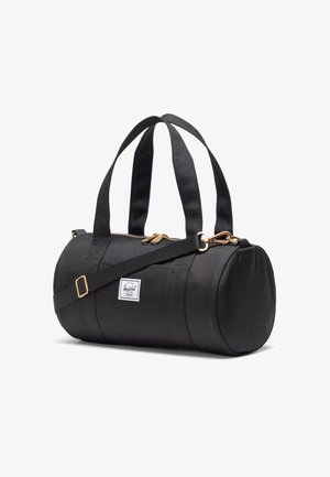 Crni cilindrični putni kofer s dvostrukim ručkama na vrhu, podesivim ramennim remenom, zlatnim patentnim zatvaračem i bijelom Herschel oznakom s strane.