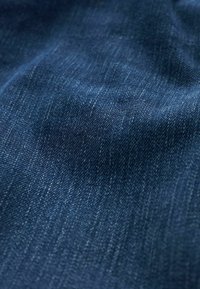 Tejido de mezclilla azul oscuro con una textura suave, que presenta ligeras variaciones en la tonalidad y un ligero brillo en la superficie.