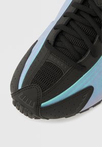 Zbliżenie na czubek czarnego buta sportowego z opalizującymi niebieskimi bocznymi panelami, czarnymi sznurowadłami i perforowanymi detalami z syntetycznej powłoki.