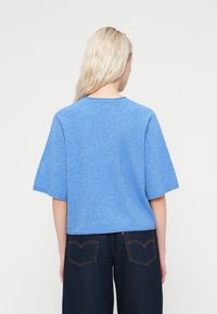 Μπλε πουλόβερ με κοντά μανίκια, υφή απαλής επιφάνειας και στρογγυλεμένο λαιμό, συνδυασμένο με σκούρο τζιν παντελόνι που διαθέτει τσέπες πίσω.