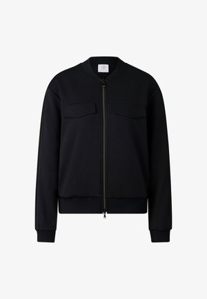 Czarna kurtka typu bomber wykonana z dzianiny dresowej, z przodu na zamek, dwie kieszenie na piersi, prążkowany kołnierz, mankiety i dół. Gładka faktura.