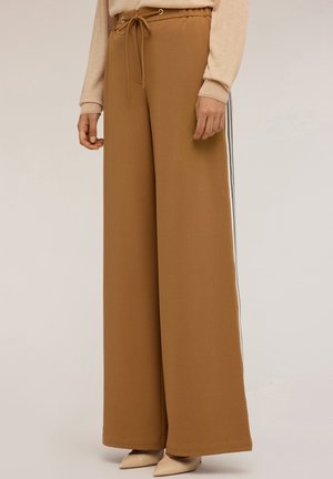 Pantaloni larghi marroni con strisce bianche e nere ai lati, cintura elastica con coulisse, indossati con un top beige a maniche lunghe e décolleté color nude a punta.