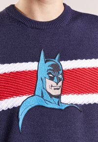 Marine gebreide trui met een geborduurd Batman-ontwerp in het blauw, met een rood-witte horizontale streep over de borst.