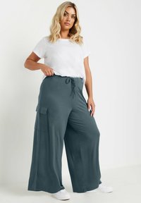 Grå vida byxor med dragsko i midjan, med en sidoficka och en mjuk, slät textur. I kombination med en enkel vit t-shirt.