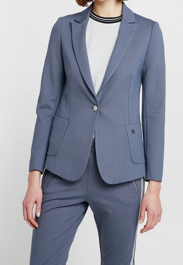 Dopasowana marynarka z miękkiego, niebieskiego materiału. Do jej szczególnych cech należą dwie przednie kieszenie, zapięcie na jeden guzik oraz klapa w stylu notch.