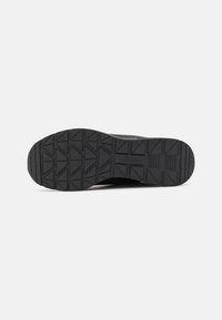 Black shoe sole with geometric tread pattern and "Skechers" brand name embossed in the center.