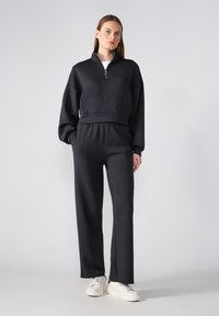 Black zip-up sweatshirt with a high collar, paired with matching loose-fit pants; both made of soft fabric with a smooth texture.
